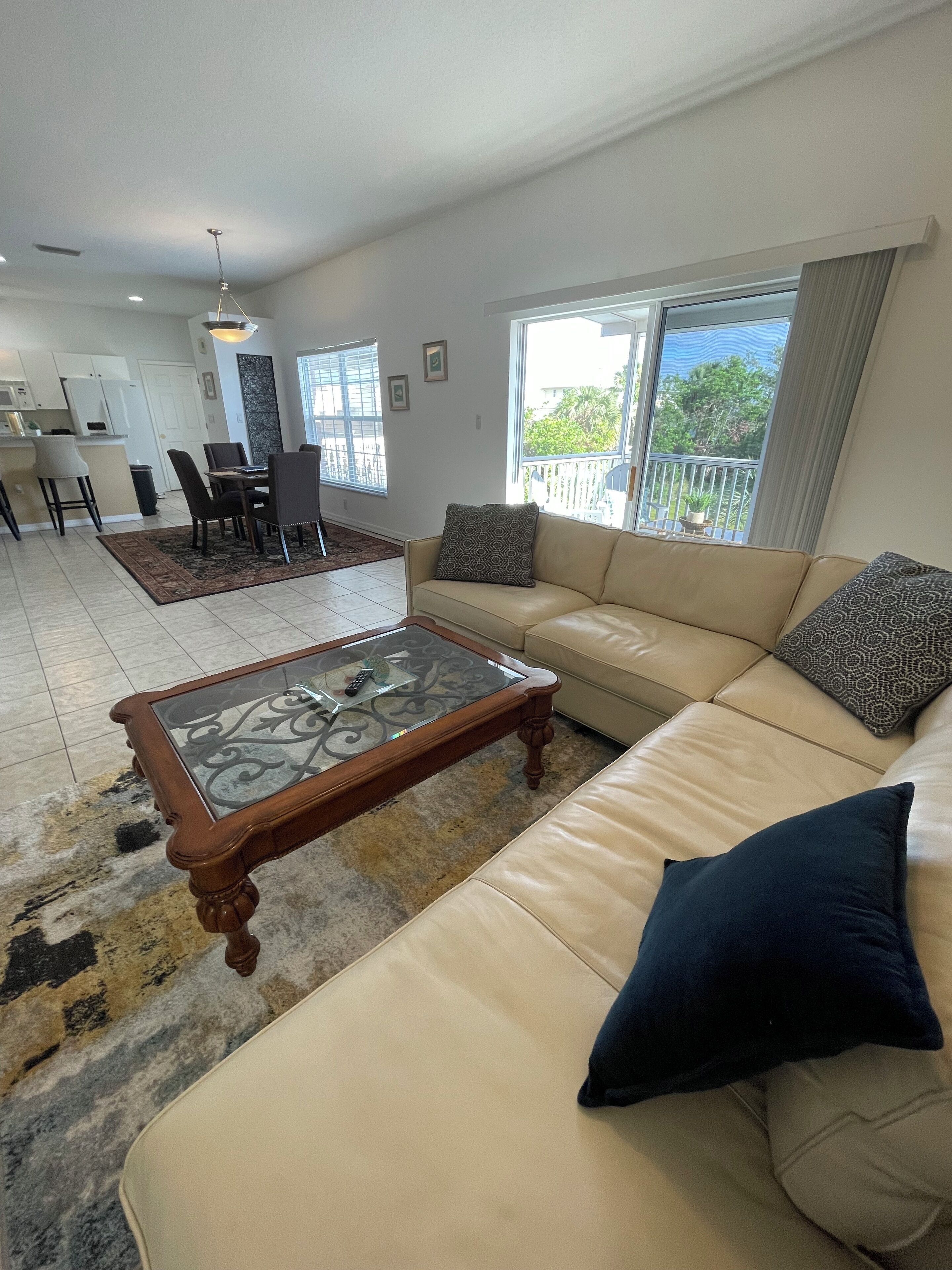 A living room with a beige sofa, a glass-top coffee table, and a view of the outdoors through large windows.