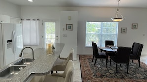 A modern kitchen with a granite countertop, stainless steel sink, and a dining area with a table and chairs. - Gorgeous condo with pool view in walking distance to Siesta Key Beaches (Sarasota)