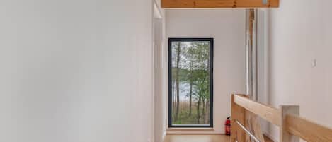 A narrow hallway with a wooden ceiling and a glass door leading to an outdoor area with trees.