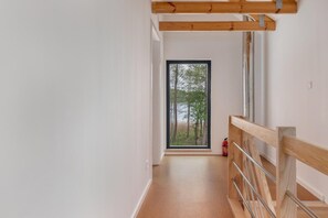 Een smalle gang met een houten plafond en een glazen deur naar een buitenruimte met bomen.