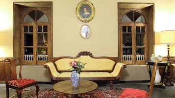 Quarto com sofá, duas cadeiras, mesa redonda, um vaso com flores e duas imagens emolduradas na parede.