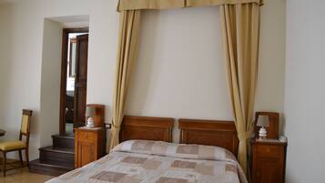 A bedroom with a bed, wooden headboard, bedside tables, a chair, and a staircase leading to another room.