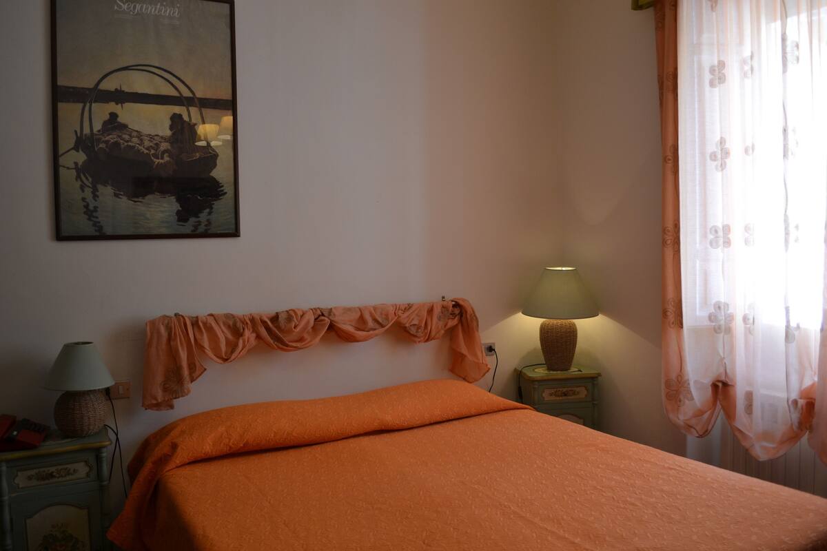 A bedroom with an orange bedspread, a lamp on a nightstand, and a wall-mounted lamp.