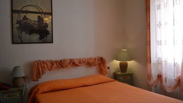 A bedroom with an orange bedspread, a lamp on a nightstand, and a wall-mounted lamp.