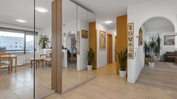 Un interior espaiós i modern amb zona de menjador, taulell de recepció i saló amb sofà i plantes.