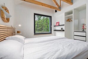 A bedroom with a large window, wooden headboard, white bedding, a bedside table with a lamp, and a wardrobe. - Holiday Home by Lake Wiselka Near Baltic Beach (gmina Wolin)