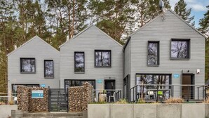 A modern two-story building with a stone wall entrance, a patio with outdoor seating, and a sign indicating 'CAYA' on the right side. - Holiday Home by Lake Wiselka Near Baltic Beach (gmina Wolin)