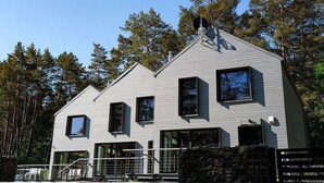 Uma casa moderna de dois andares com telhado empena e janelas amplas, e um quintal cercado.