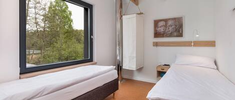 A bedroom with two beds, a window, a wooden ceiling, and a painting on the wall.