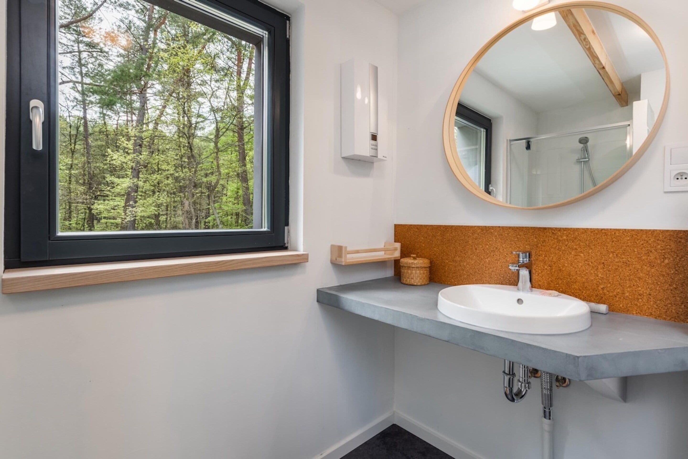 A bathroom with a window, a sink, a mirror, and a shower.