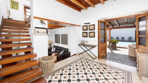 Ein modernes Interieur mit einer Holztreppe, einem schwarzen Ledersofa, einem gemusterten Teppich und Blick auf einen Pool.