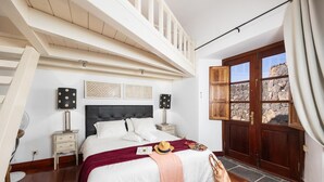 Ein Schlafzimmer mit Bett, Nachttischen, einem Fenster mit Blick auf eine Steinmauer und einem Balkon mit Holzgeländern.