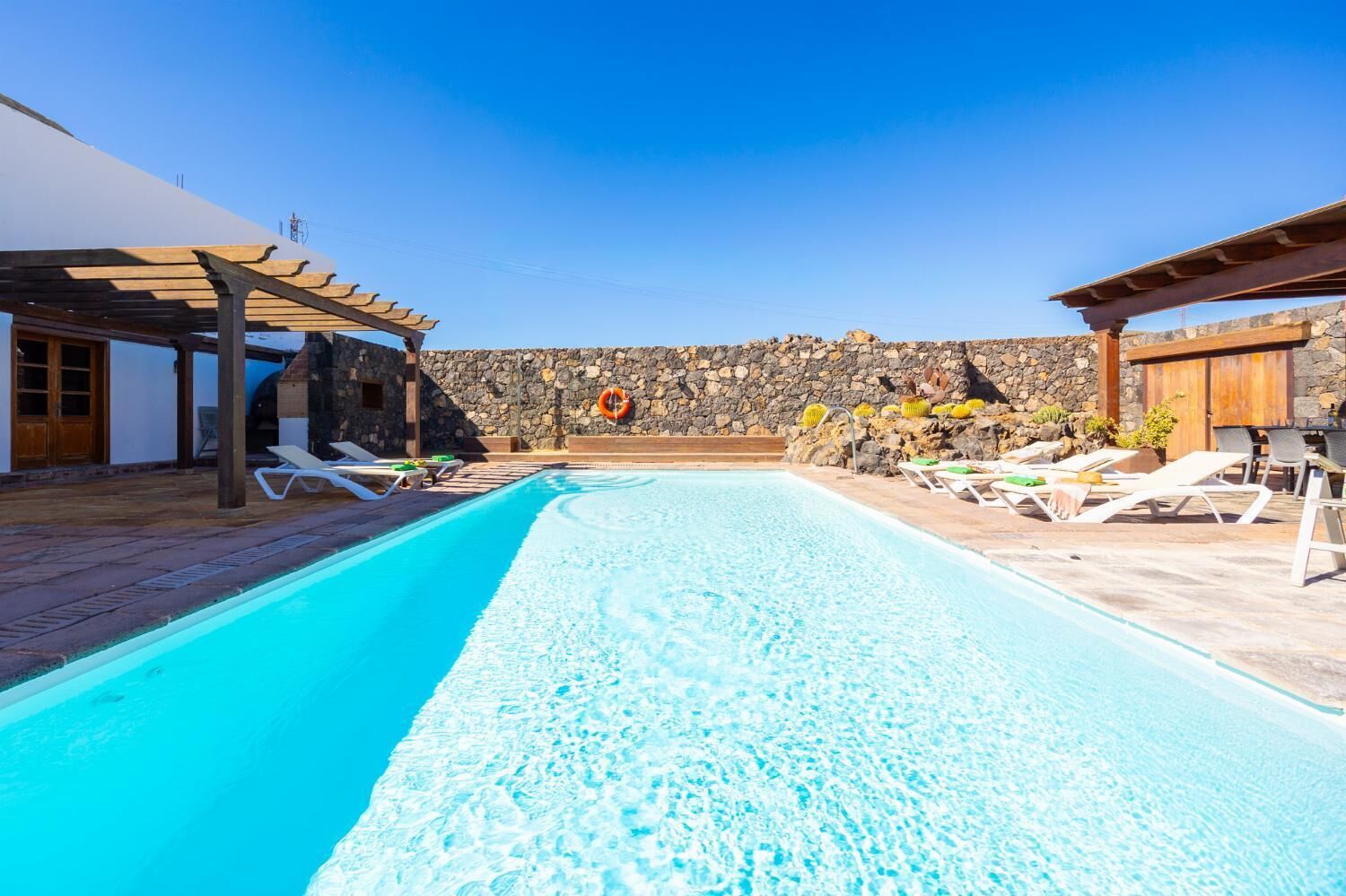 Une piscine avec des chaises longues et un mur de pierre en arrière-plan.