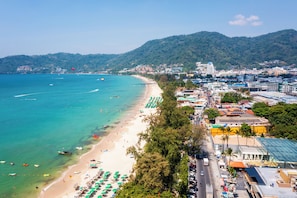 Un paisaje urbano costero con una playa, aguas azules cristalinas y un fondo montañoso.