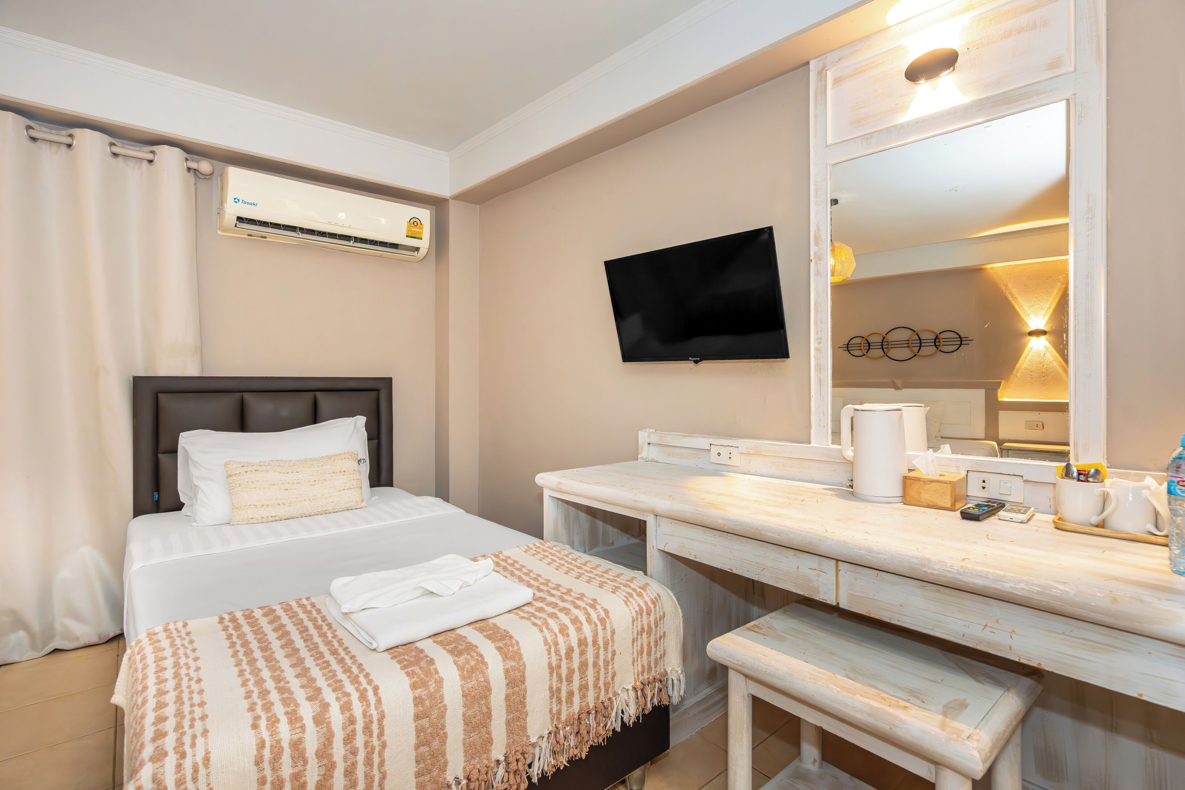 Une chambre d’hôtel équipée d’un lit, d’une table de chevet, d’un miroir, d’une télévision et d’un appareil de climatisation.