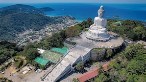 Una gran estatua blanca de Buda rodeada por un paseo circular, con vistas a un pueblo costero y montañas al fondo.