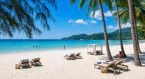 A beach with lounge chairs, palm trees, and clear blue water. - The Taksim Patong Beach Hotel (Patong)