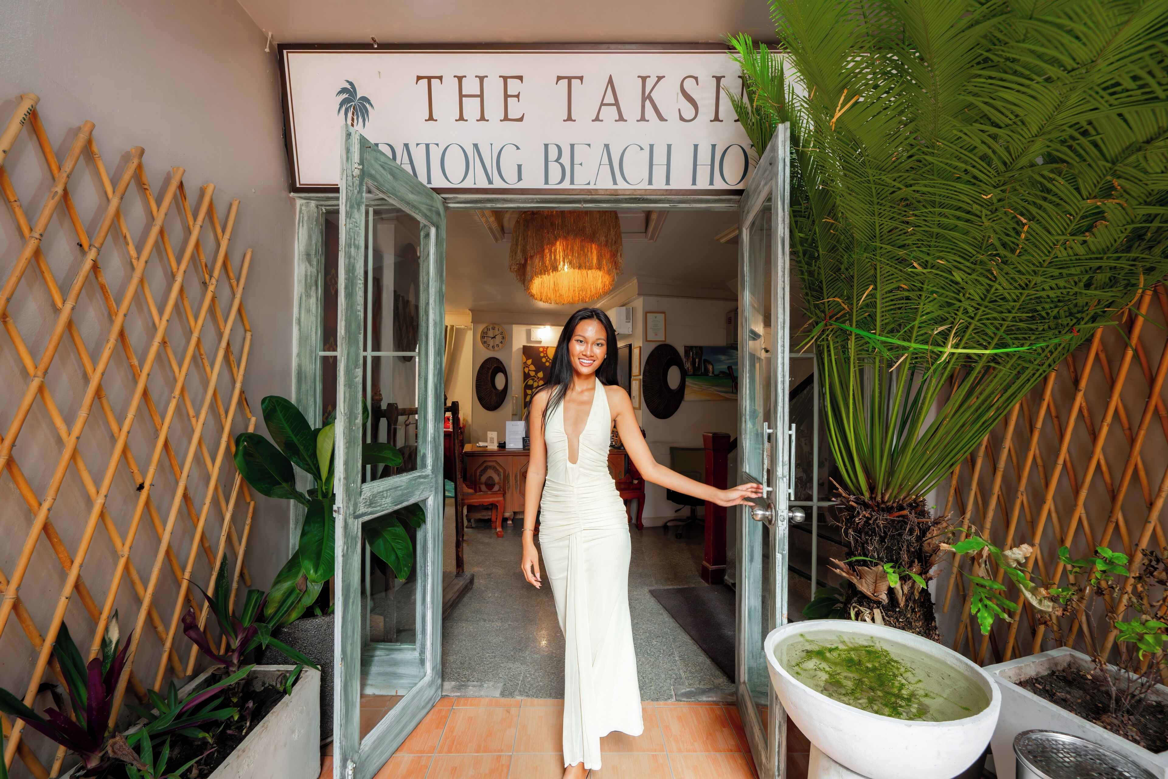Una mujer con un vestido blanco parada en la entrada del hotel 'The Taksi Patong Beach Hotel'.