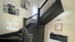 Una escalera con barandales oscuros y un pasamanos negro que conduce a un rellano con una consola negra y una obra de arte enmarcada.