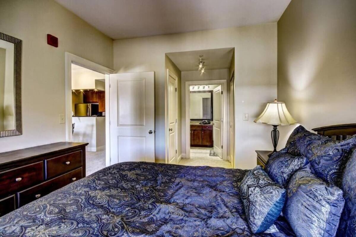 A bedroom with a large bed, a dresser, a lamp, and an open door leading to a hallway.