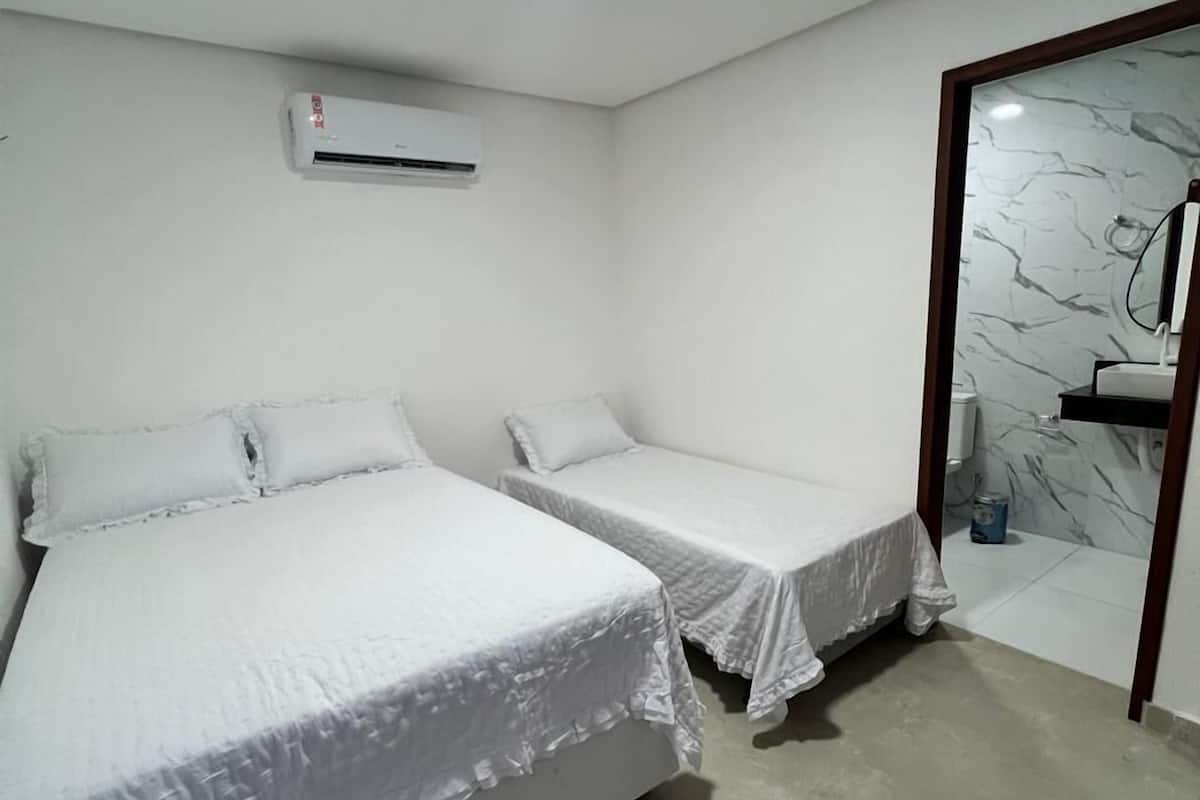 A hotel room with two single beds, a bathroom with a marble wall, and an air conditioning unit on the wall.