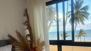 Habitación de hotel con un ventanal amplio que ofrece vistas a la playa y palmeras.