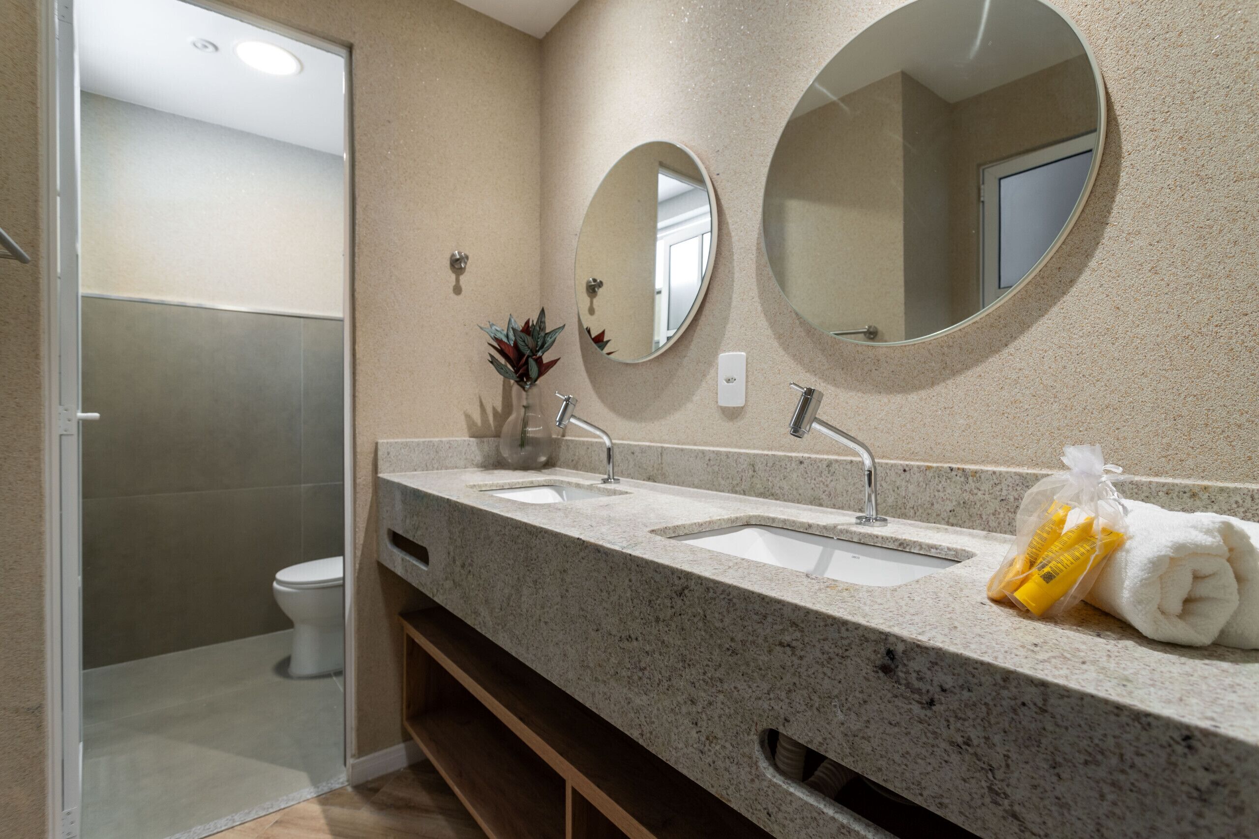 A modern bathroom with a granite countertop, two sinks, a large mirror, and a shower area.