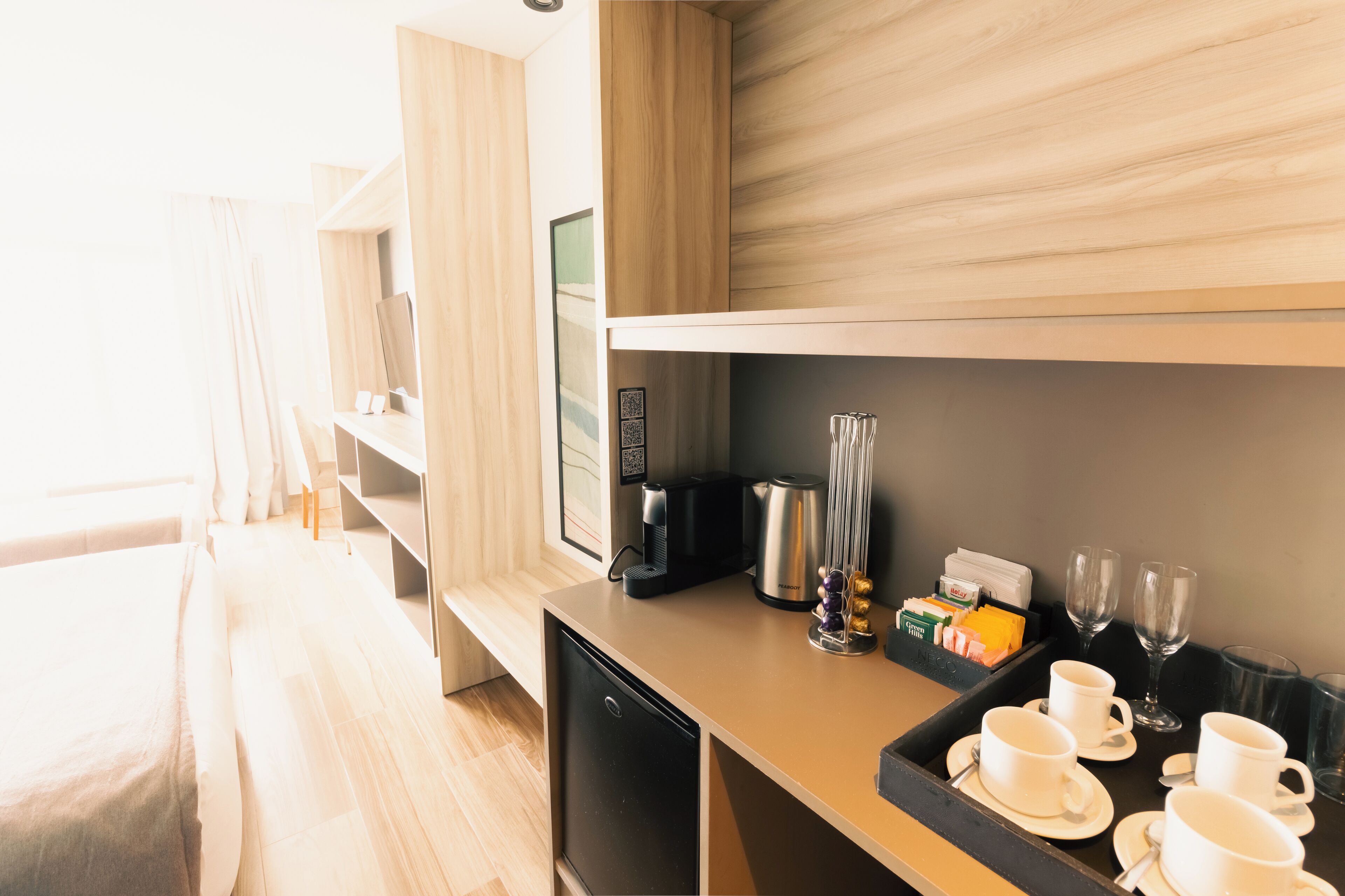 Una habitación de hotel moderna con kitchenette, una cama y una bandeja de desayuno con tazas y cafetera.