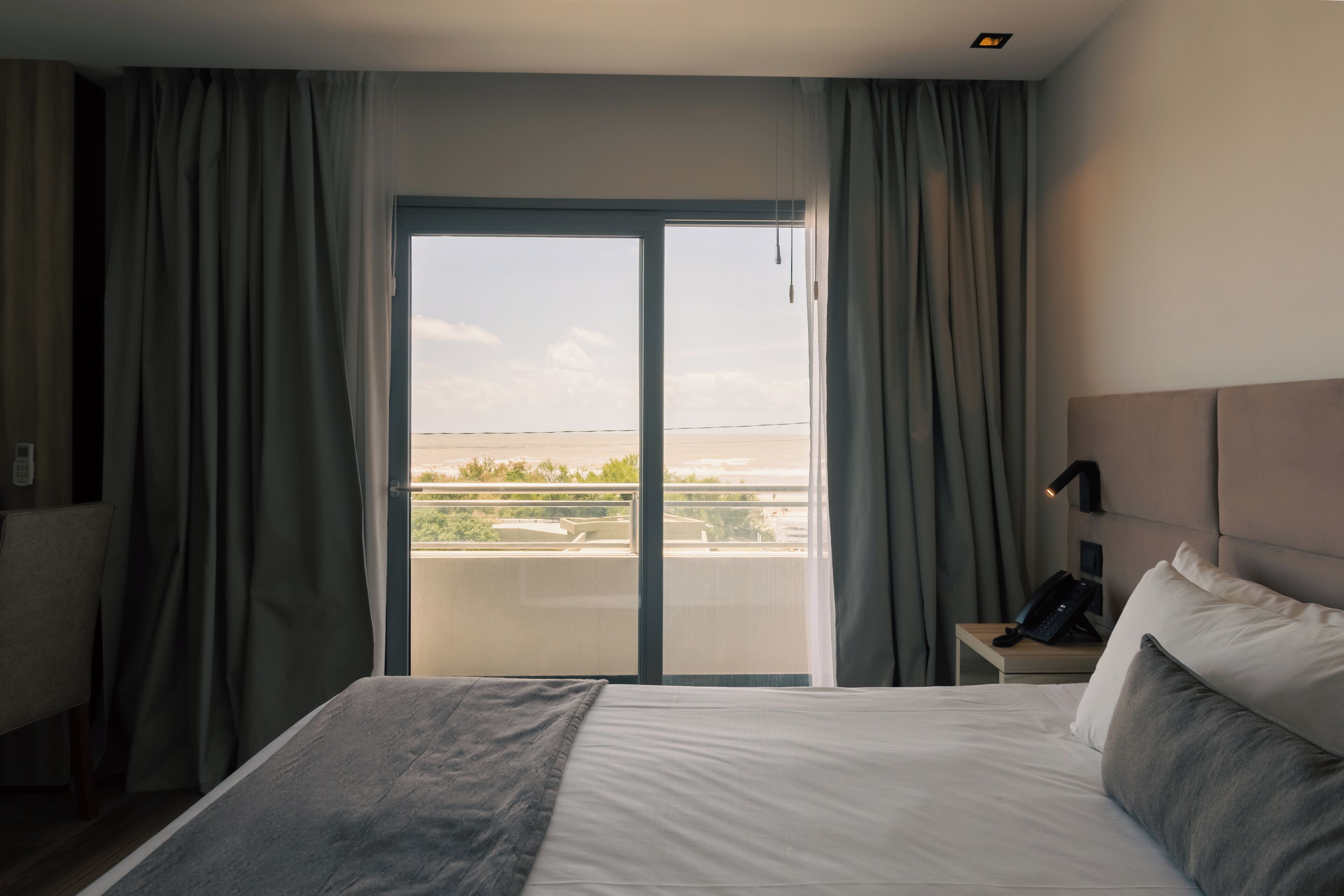 Habitación de hotel con cama, mesita de noche con teléfono y vista a través de un ventanal grande.