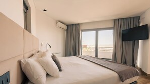 A modern hotel room with a large bed, a flat-screen TV mounted on the wall, and a view of the city through the window.