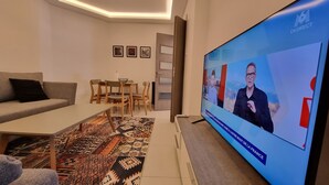 A modern living room with a television displaying a news program, a sofa, a coffee table, and a patterned rug. - Modern & Restful, Akid Lotfi Oran  (Oran)