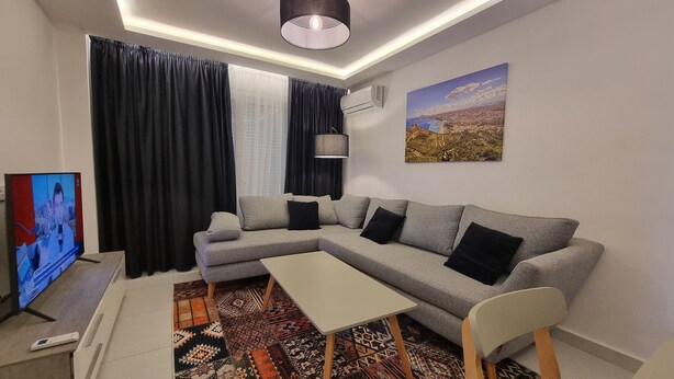 A modern living room with a grey sectional sofa, a small white table, and a patterned rug. - Modern & Restful, Akid Lotfi Oran  (Oran)
