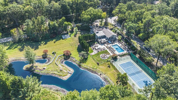 An aerial view of a property with a swimming pool, tennis court, and landscaped areas.