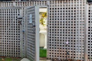 A wooden gate with a sign, leading to a white bathtub and a small garden area with a flamingo statue.