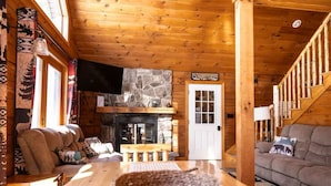 Ein gemütliches Blockhaus-Interieur mit Kamin aus Stein, Holzwänden, einer Couch und einem Esstisch.