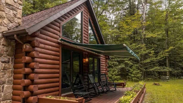 Eine Blockhütte mit Veranda, Sitzgelegenheit im Freien und einer Steinsäule.
