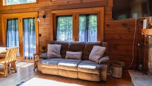 Ein gemütliches Blockhaus-Interieur mit einer Couch, Holzwänden und großen Fenstern.