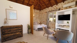 A room with a stone wall, a bed, a TV, and a wooden dresser. - vigla vilas  (Zakynthos)