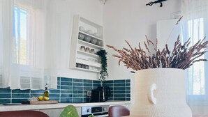 A kitchen with a wooden table, a white vase with dried plants, and a window with curtains. - vigla vilas  (Zakynthos)
