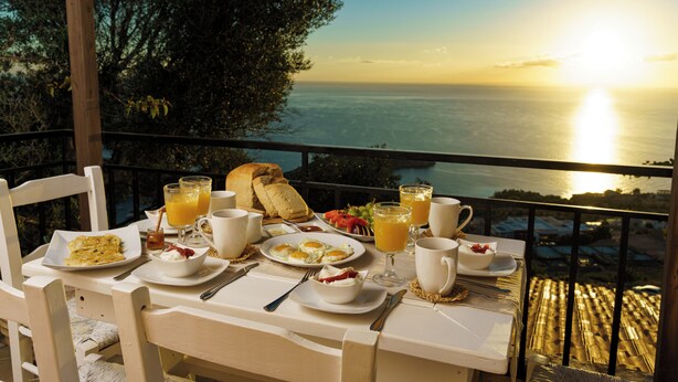 A breakfast table with plates of food, glasses of orange juice, and a view of the sea at sunrise. - vigla vilas  (Zakynthos)