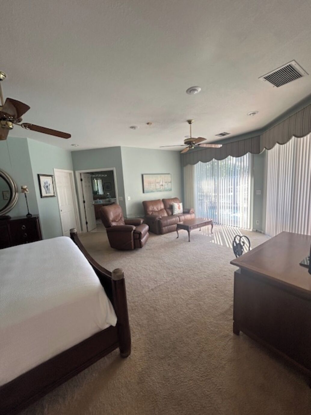 A bedroom with two beds, a chair, a sofa, a desk, and a ceiling fan.