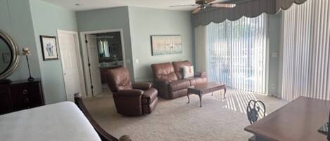 A bedroom with two beds, a chair, a sofa, a desk, and a ceiling fan.