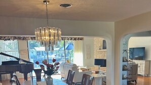 Un comedor amplio con una larga mesa de madera y sillas, una araña y un piano al fondo.