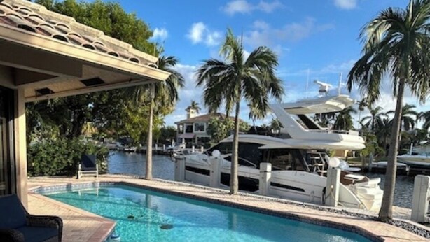 Una piscina con zona de patio, un muelle para barcos y una casa al fondo.