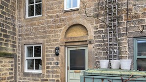 A stone building with a white door, a window, and a small garden area with a plant pot. - 2 bedroom accommodation in Addingham, near Ilkley (Addingham, near Ilkley)