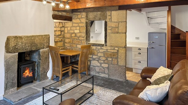 A cozy living room with a stone fireplace, leather sofa, and a dining area with wooden chairs. - 2 bedroom accommodation in Addingham, near Ilkley (Addingham, near Ilkley)