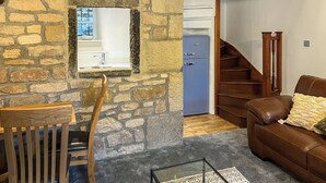 A stone-walled room with a wooden chair, a brown leather sofa, a small table, a blue refrigerator, and a wooden staircase. - 2 bedroom accommodation in Addingham, near Ilkley (Addingham, near Ilkley)