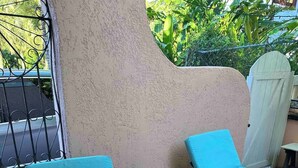 Un'area patio con due poltrone blu imbottite e un tavolo con piano in vetro, circondata da un muro strutturato e un cancello in metallo.