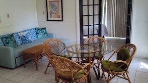 A dining area with wicker chairs and a glass table, a light-colored sofa with patterned cushions, and a ceiling fan. - Condo - 2 beds with WiFi, AC, Pool and Oceanfront in charming Frigate Bay. (Frigate Bay)