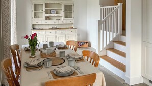 A dining area with a table set for four, surrounded by wooden chairs. A white cabinet with glass doors is visible in the background. - 2 bedroom accommodation in Clevedon (Clevedon)